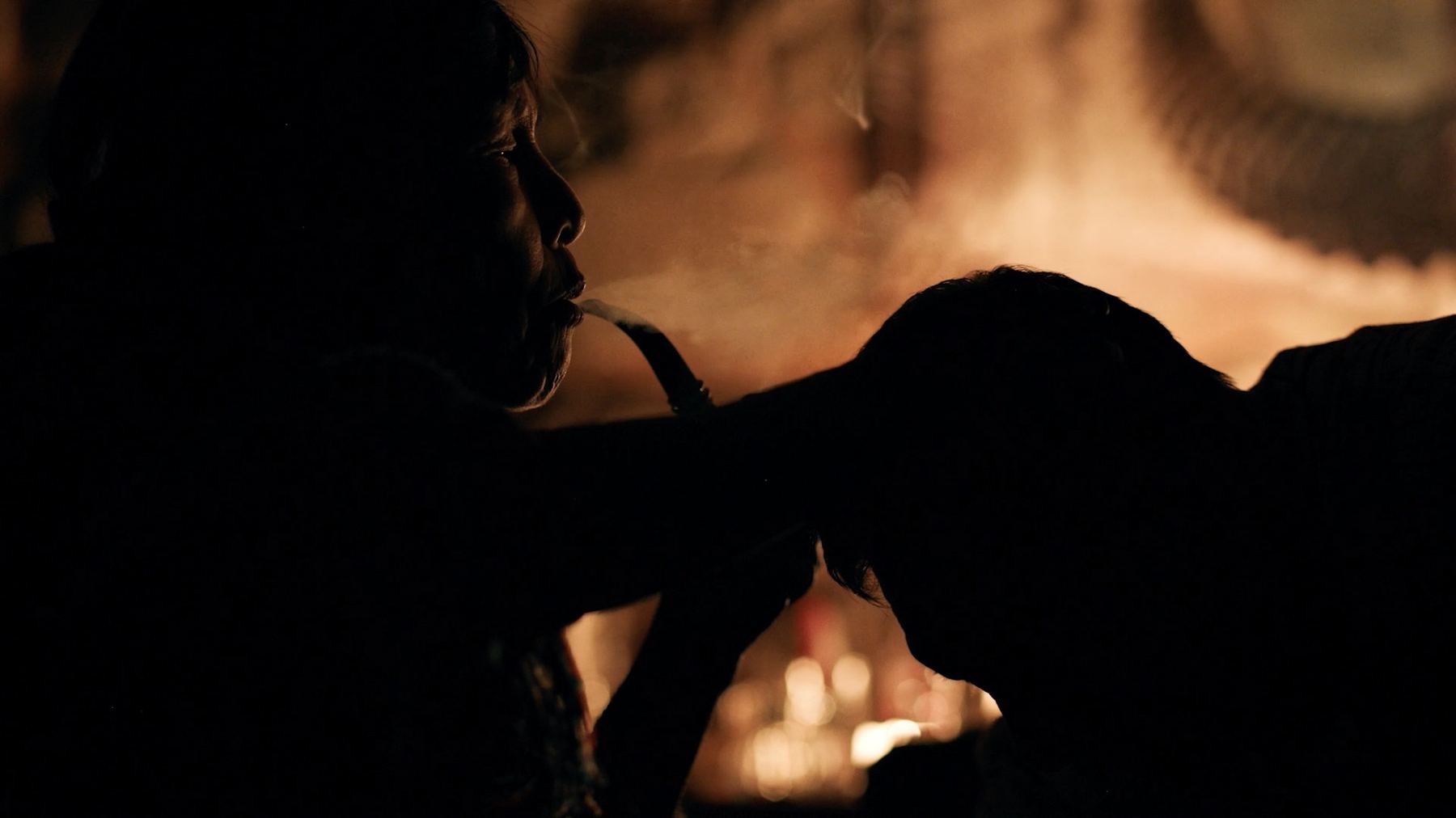 A shaman in silhouette against candlelight during ceremony